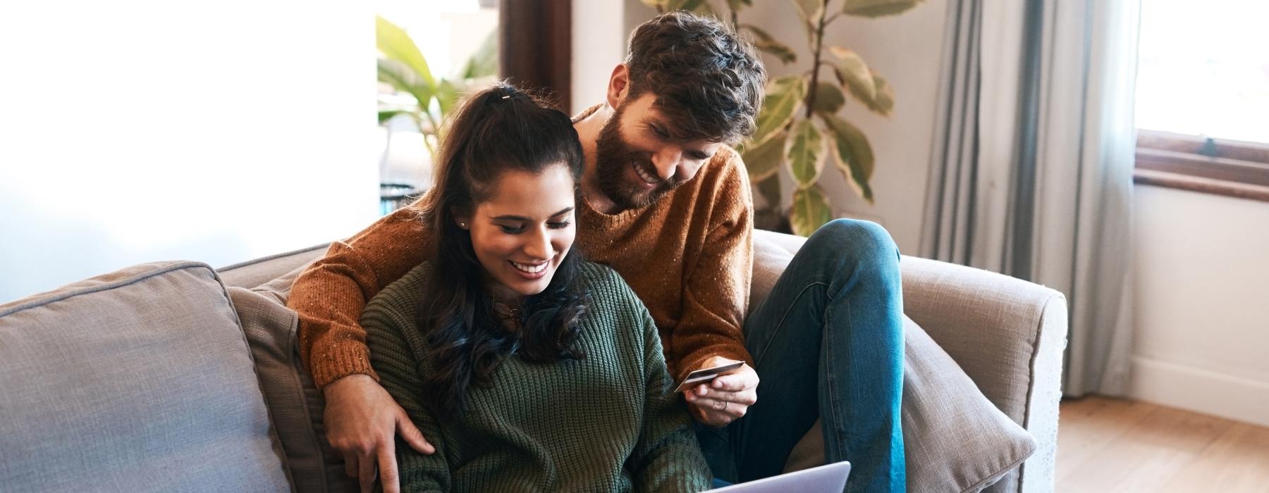 a man and woman sitting on a couch looking at a laptop